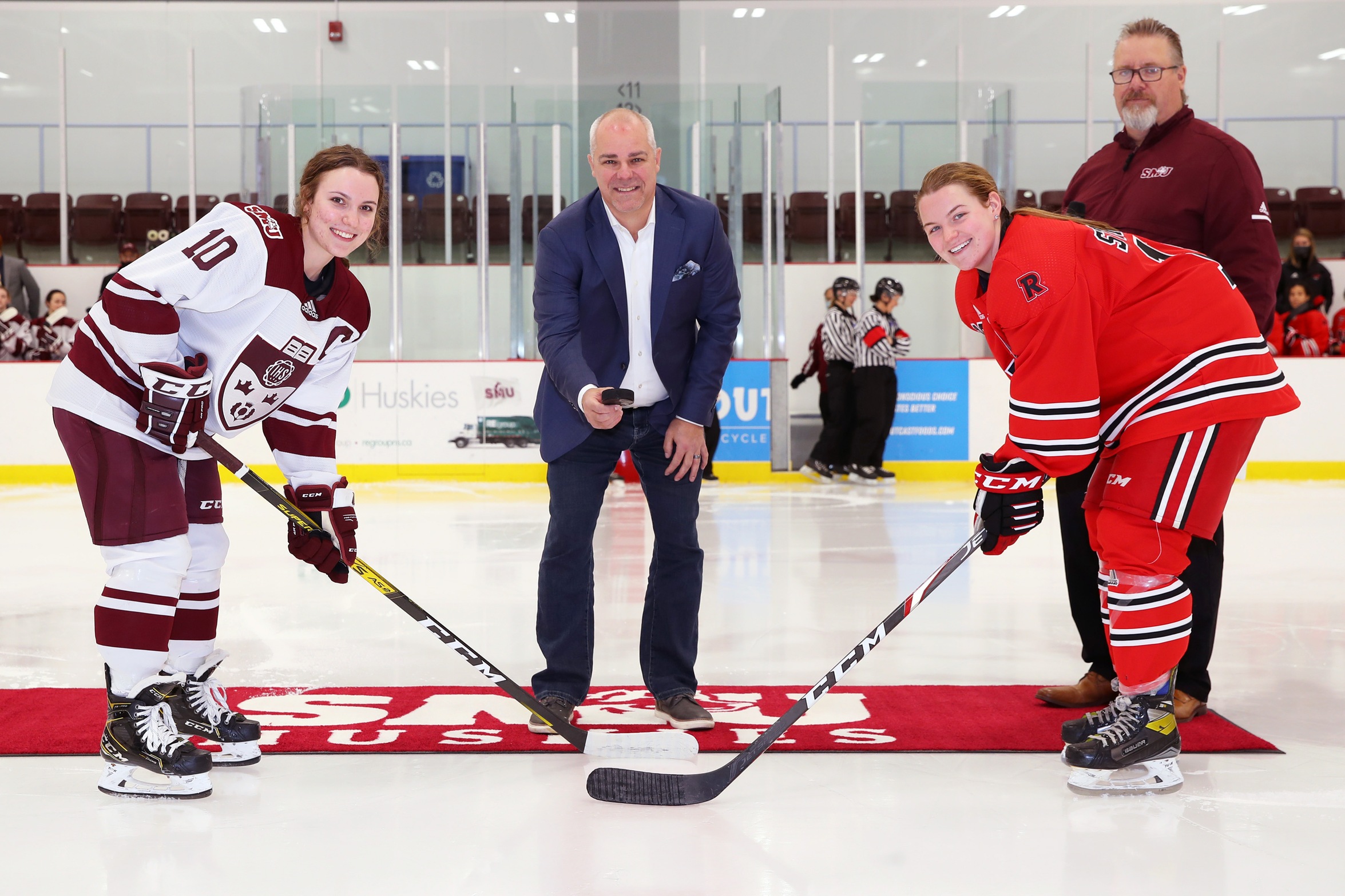 Marc Warner, son of late Huskies legend Bob Warner ('75), drops the ceremonial pre-game faceoff between Huskies captain Alexa McMillan (left) and UNB REDS Ashley Stratton (right), as Saint Mary's Athletic Director Scott Gray looks on.
